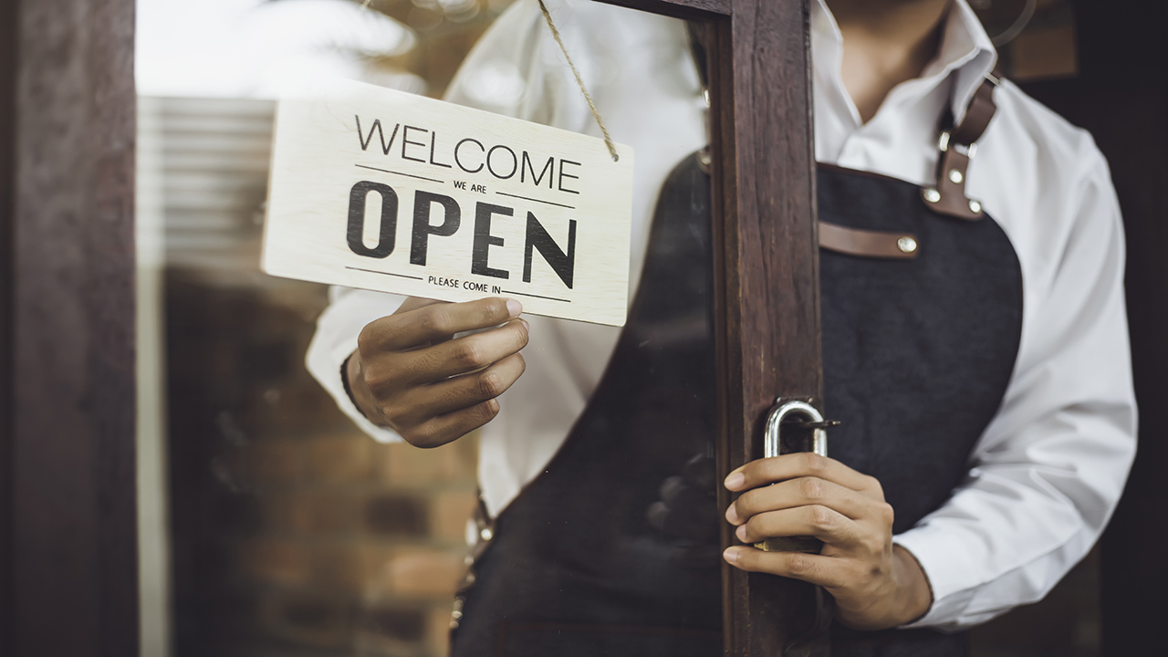 Person wearing an apron changing an Open sign on a glass door